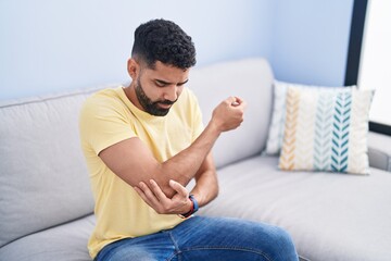 Young arab man sitting on sofa suffering for elbow pain at home