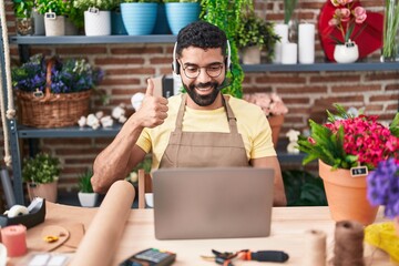 Hispanic man with beard working at florist shop doing video call smiling happy and positive, thumb...