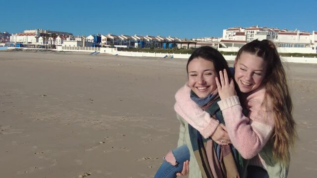 Happy female friends enjoying piggyback ride on beach