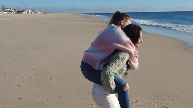 Happy female friends enjoying piggyback ride on beach