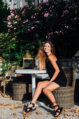 Fototapeta na wymiar Beautiful slender fashionable woman in black summer dress sitting on bench