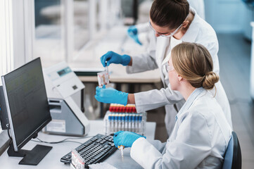 team of laboratory technicians conduct series of tests on  chemical analyzer in laboratory. Two female scientists work in modern equipped computer laboratory doing tests with tubes and pipette
