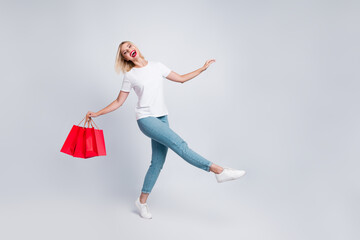 Full size photo of funny optimistic woman dressed white t-shirt denim pants walking with shopping...