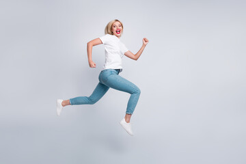Fototapeta na wymiar Full size photo of adorable energetic woman dressed white t-shirt denim pants run in empty space isolated on white color background