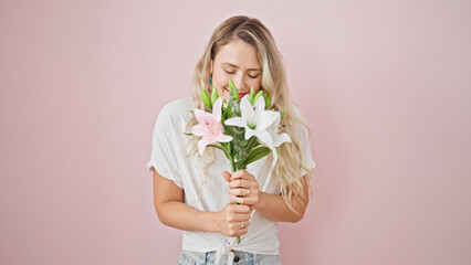 Young blonde woman smelling bouquet of flowers over isolated pink background