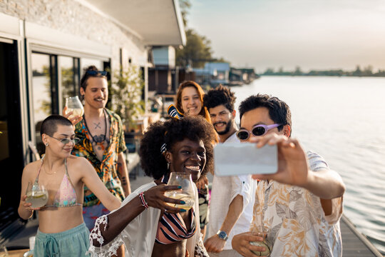 Young friends taking selfie lakeside having drinks
