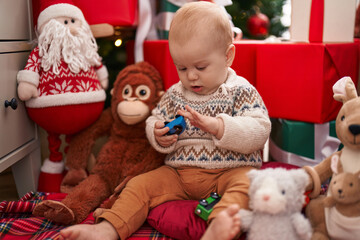Fototapeta na wymiar Adorable caucasian baby playing with car toy sitting on floor by christmas gifts at home