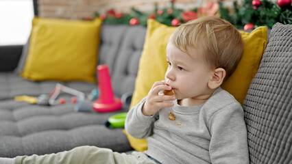 Caucasian toddler sitting on the sofa eating cookies at home