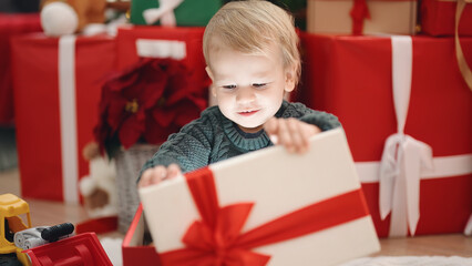 Adorable blond toddler unpacking christmas gift sitting on floor at home