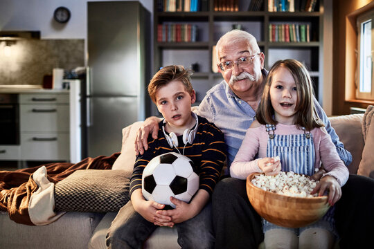 Grandfather watching a football game with his grandchildren at home