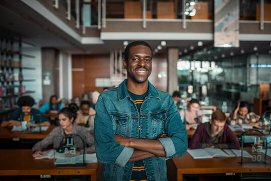 Confident young man standing in university library looking at camera