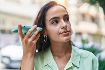 Young beautiful hispanic woman listening audio message by the smartphone at street