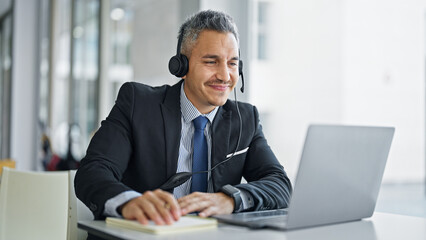 Young hispanic man business worker using laptop and headphones smiling at office