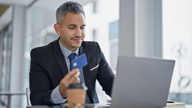 Young hispanic man business worker using laptop holding credit card at office