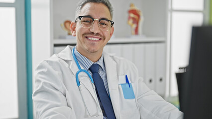 Young hispanic man doctor using computer wearing glasses at clinic