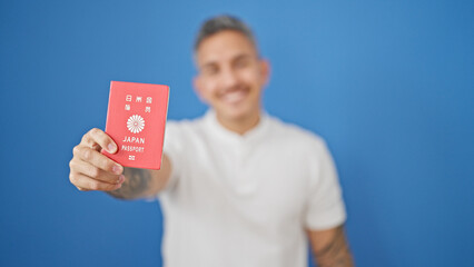 Young hispanic man smiling confident holding japan passport over isolated blue background