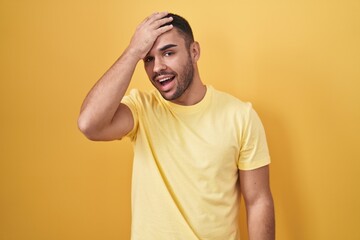 Fototapeta na wymiar Young hispanic man standing over yellow background surprised with hand on head for mistake, remember error. forgot, bad memory concept.