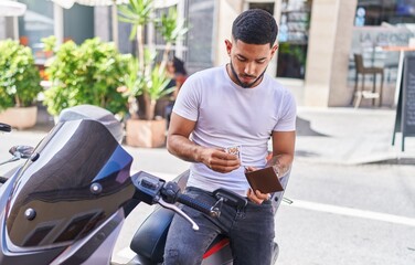 Fototapeta na wymiar Young latin man counting dollars sitting on motorbike at street