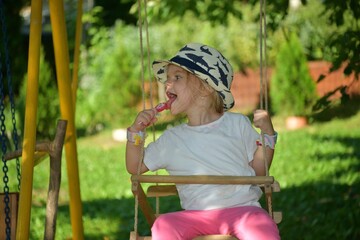 A little girl in a hat is swinging on a swing hung on a tree in the garden