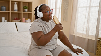 Confident african american woman enjoying morning, relaxing on bed singing to a song using a brush...