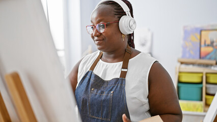 Confident african american woman artist drawing with passion, listening to music in art studio,...