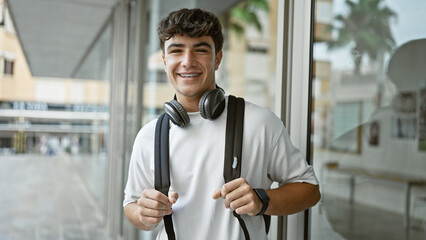 Cheerful young hispanic male student standing outdoors enjoying campus life, confidently wearing...