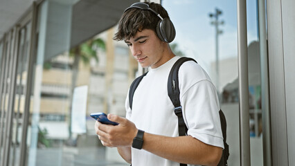 Cool young hispanic guy, a serious university student, vibing to music on his smart-phone, lost in...