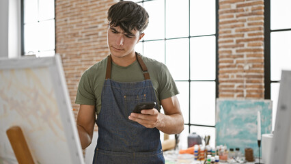 Inspiring sight, handsome, relaxed hispanic teenager engrossed in drawing on smartphone at art...