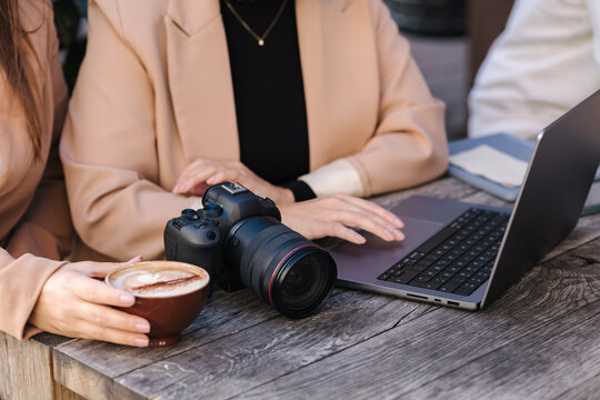 Middle selection of two women drinks coffee in cafe and checking pictures at the laptop. Mirrorless camera on table