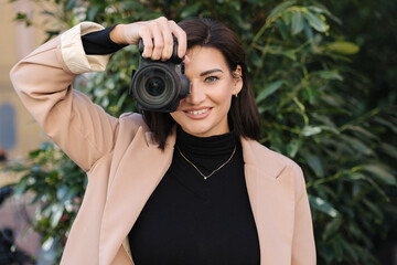 Portrait of woman photographer with mirrorless camera taking pictures outdoor. Young attractive...