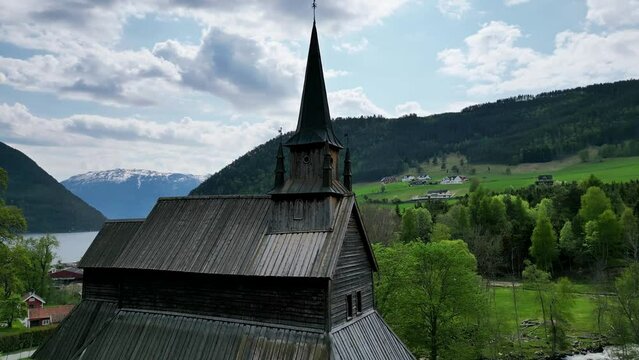 Norwegian stave church and grave yard in the mountain village of Kaupanger. Fjord and snowy mountains in the background. Filmed by drone in 4K.
