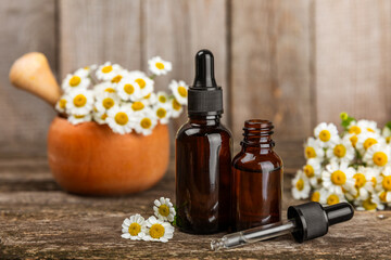Glass bottle with chamomile essential oil on an old wooden background. Chamomile flowers, close up. Aromatherapy, spa and herbal medicine ingredients. Beauty concept.Copy space. Natural cosmetic