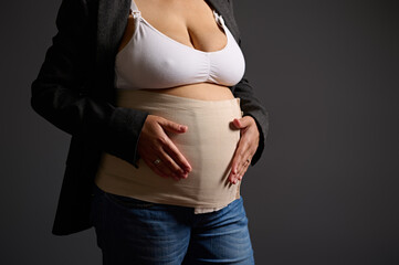 Cropped view of a young woman wearing elastic bandage on her postnatal belly, smiling looking at...