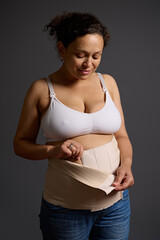 Middle aged woman putting on elastic bandage after surgical operation cesarean section, isolated...