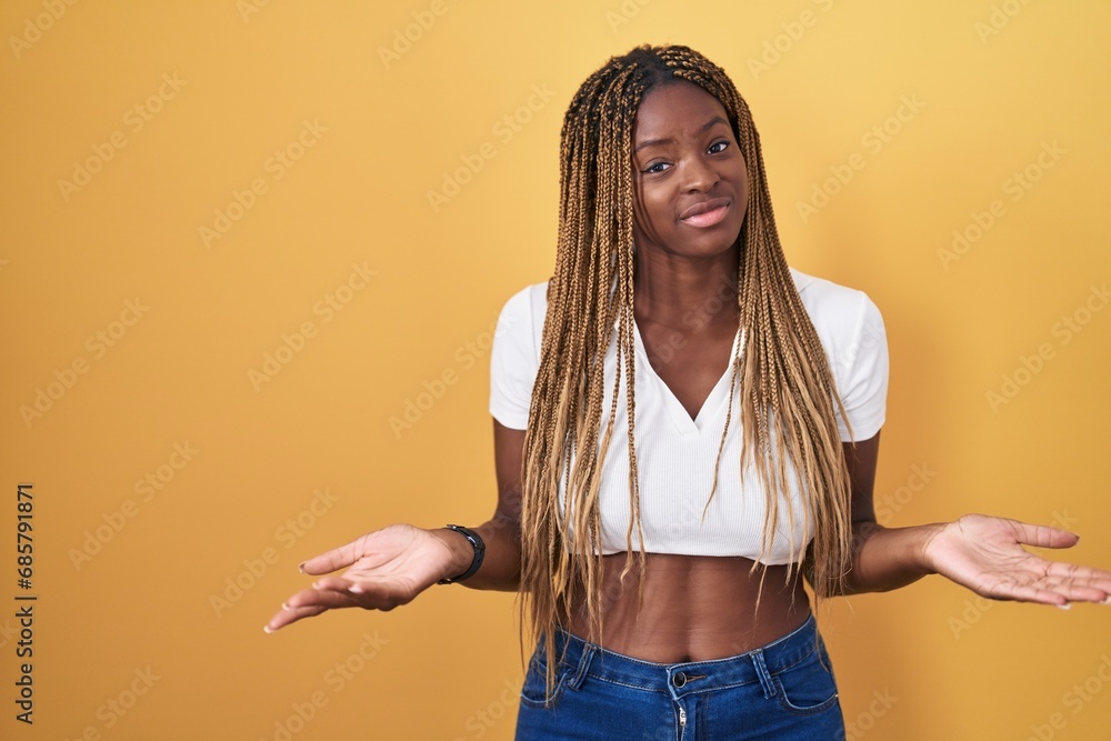 Canvas Prints African american woman with braided hair standing over yellow background clueless and confused with open arms, no idea concept.