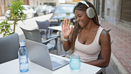 African american woman having video call sitting on table at coffee shop terrace