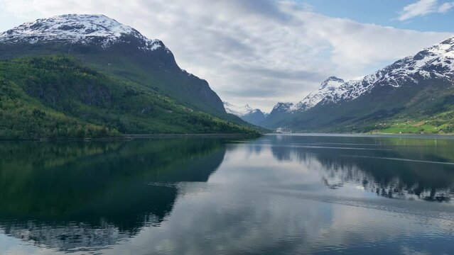 Fjord in Norway with reflective snowy mountains and cruise ship. Port town filmed by drone in 4K.