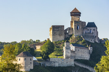 Trenčín castle with walls standing on a hill, surrounded by greenery and illuminated by the...