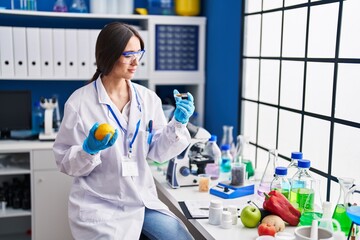 Young beautiful hispanic woman scientist holding lemon and pills at laboratory