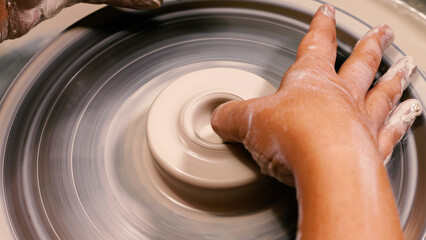 A woman's stained hand forms a blank cup from clay on a potter's wheel. Work in a pottery workshop. The concept of manual labour, art and craft.