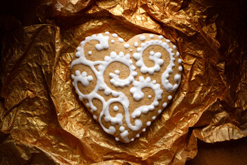 Traditional heart-shaped gingerbread cookie decorated with white icing on a golden background,...