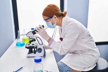 Young caucasian woman scientist wearing medical mask using microscope at laboratory