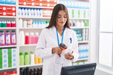 Young beautiful hispanic woman pharmacist scanning pills bottle at pharmacy