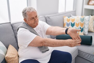 Middle age grey-haired man stretching arm sitting on sofa at home