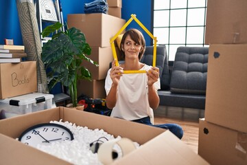 Brunette woman sitting on the floor at new home holding ruler smiling looking to the side and...