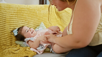 Joyful mother and daughter lying on sofa, laughing a lot while having tickle play at home