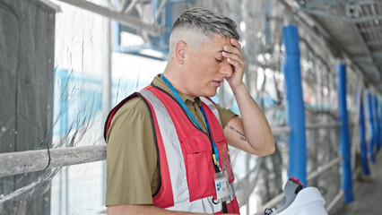 Young caucasian man builder taking hardhat off sweating at construction place