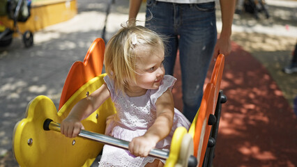 Caucasian mother and willing daughter sitting on a seesaw, playing seriously in the park playground...