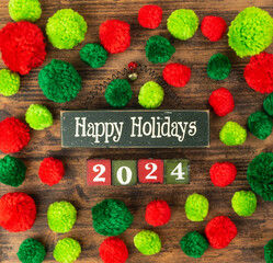 Red and green pompoms with wooden blocks and text happy holidays and 2014 on wood