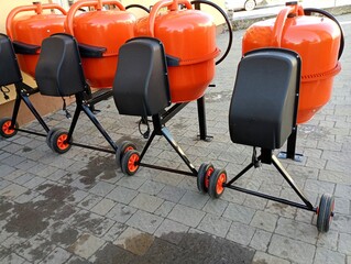 A number of new orange concrete mixers are for sale outside on a cobblestone site. The topic of...